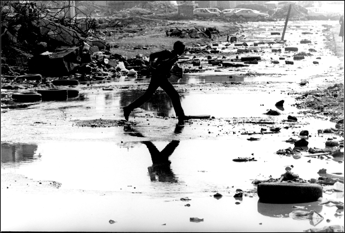 Sabra Palestinian camp. Young boy jumps over puddle in the camp's main street. 1982 : Lebanon 1981-2008 : BILL FOLEY 