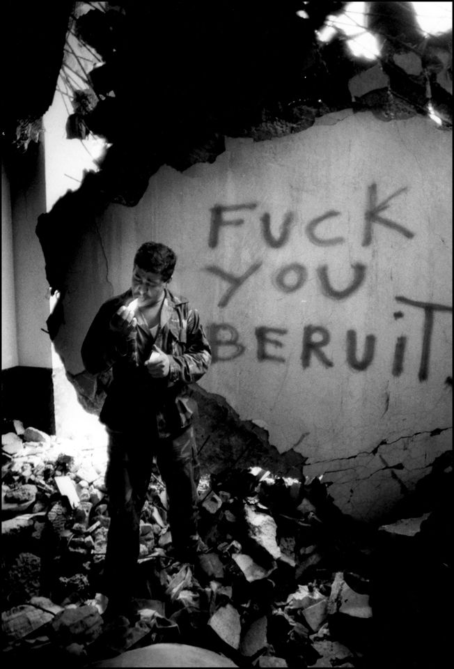 Oct. 23, 1984-One year Later, Lebanese soldier lights a cigarette in the basement of the US Marine HQ that was destroyed in a truck bomb attack, Oct. 1983. Departing Marine left message behind. : USMC in Beirut 1982-1983 : BILL FOLEY 